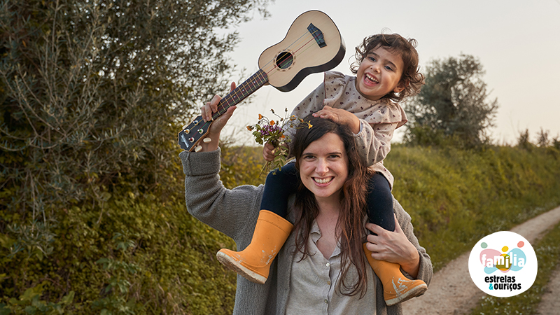 Criança nas cavalitas da mãe com um ukulele